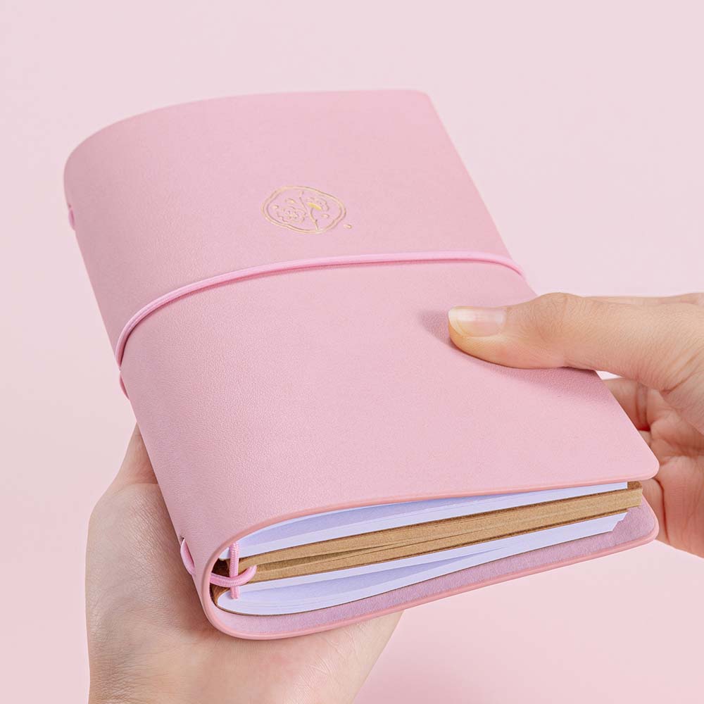 Tsuki ‘Sakura Journey’ Limited Edition Travel Notebook held in hands at an angle in pink background