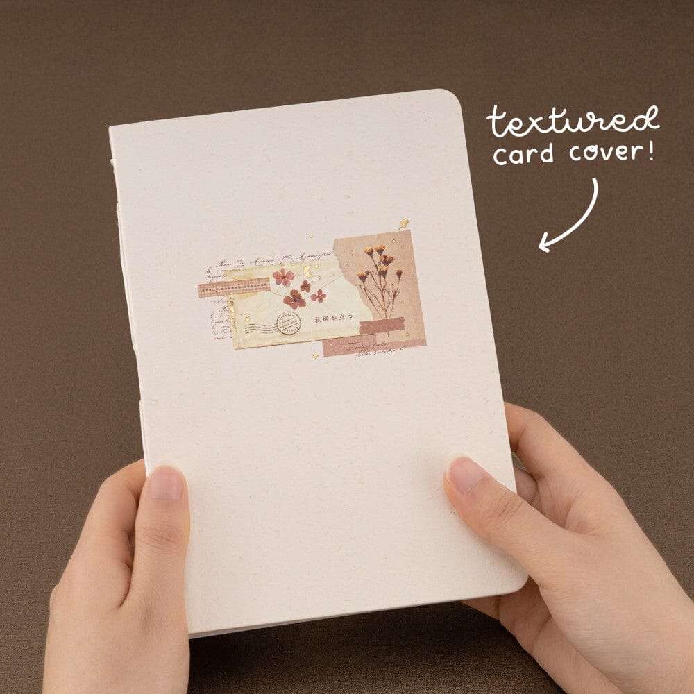 Hands holding the Junk Journal notebook with white text “textured card cover”