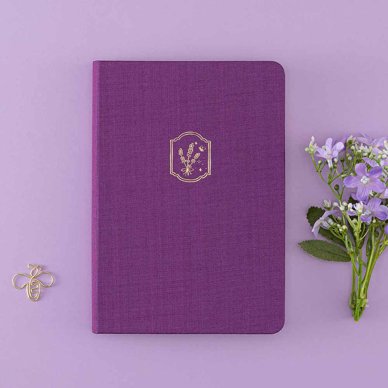 Tsuki ‘Enchanted Garden’ lavender foil design on purple linen bullet journal on purple background with bee shaped paper clip and purple flower