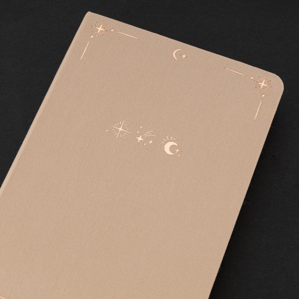 Close up of Tsuki Stardust Dawn Bullet Journal beige linen cover with rose gold design with crescent moon and stars around it