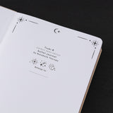 Close up of Tsuki Stardust Dawn Bullet Journal beige linen cover with rose gold design with crescent moon and stars around it