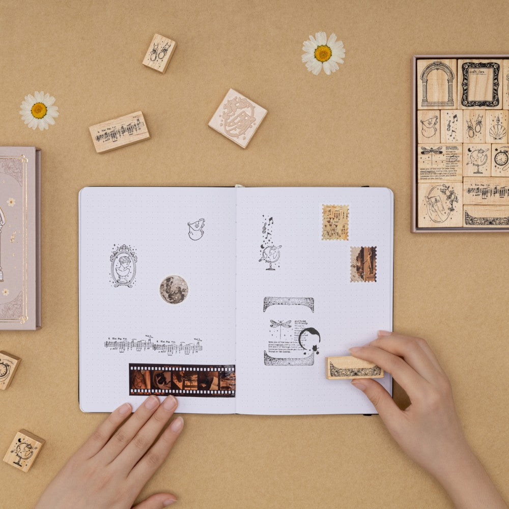 Hands stamping a border stamp on bullet journal with other Light Academia stamps