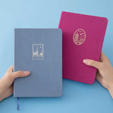 A pair of hands holding a Tsuki Kyoto bullet journal and Tokyo bullet journal