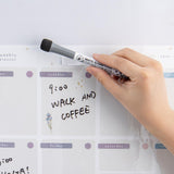 Close up of Tsuki Reusable Weekly Planner with whiteboard marker eraser and sticky pen holder held in hand on light grey surface