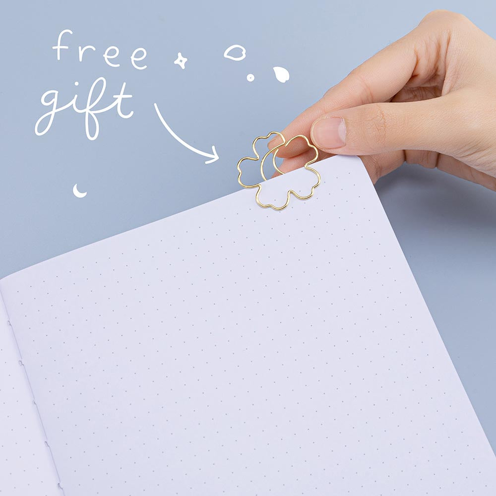 Close up of open page of Tsuki ‘Lunar Blossom’ Limited Edition Bullet Journal with free bookmark gift held in hand in light blue background