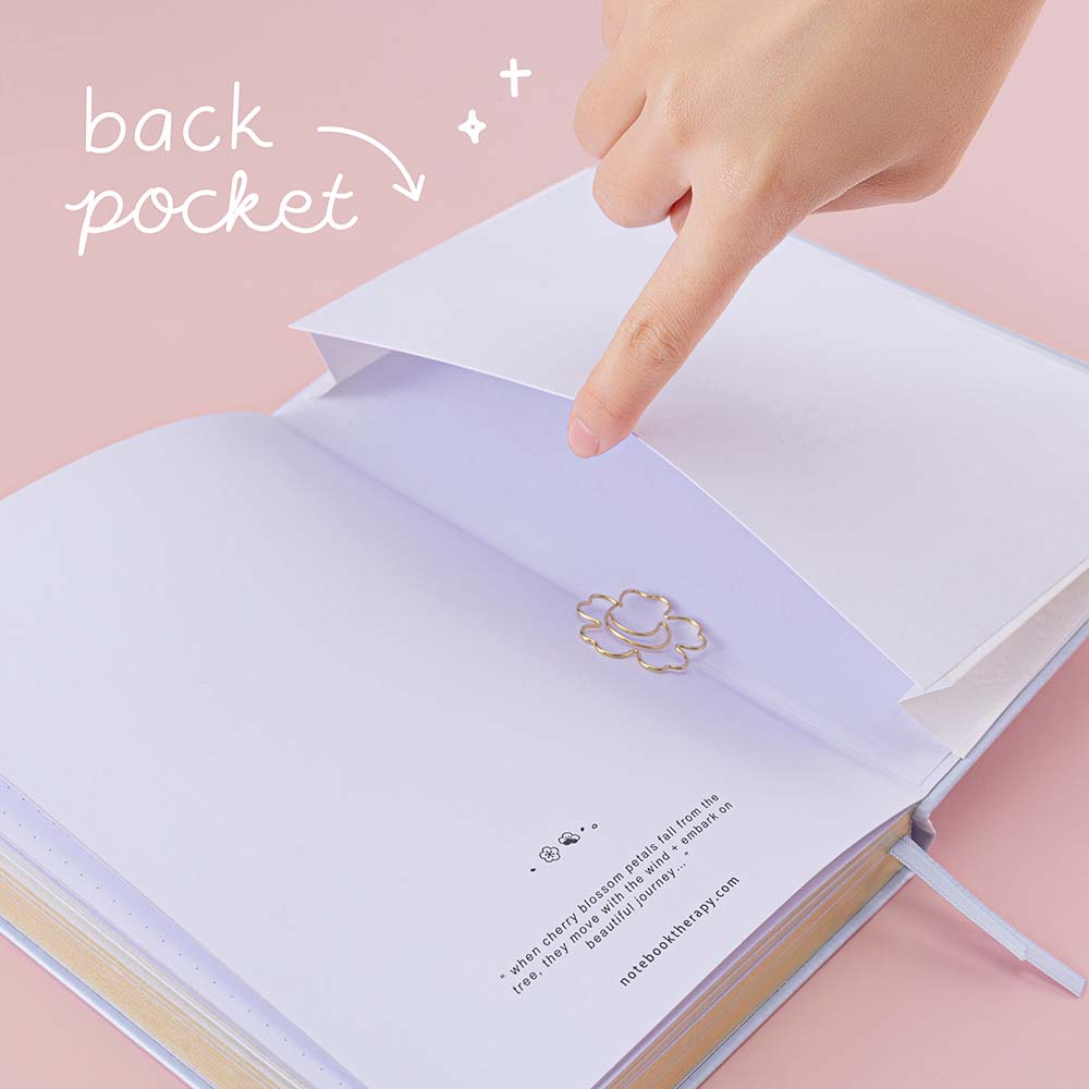 Open back page pocket of Tsuki ‘Sakura Journey’ Limited Edition Bullet Journal held in hand with free bookmark gift on pink background
