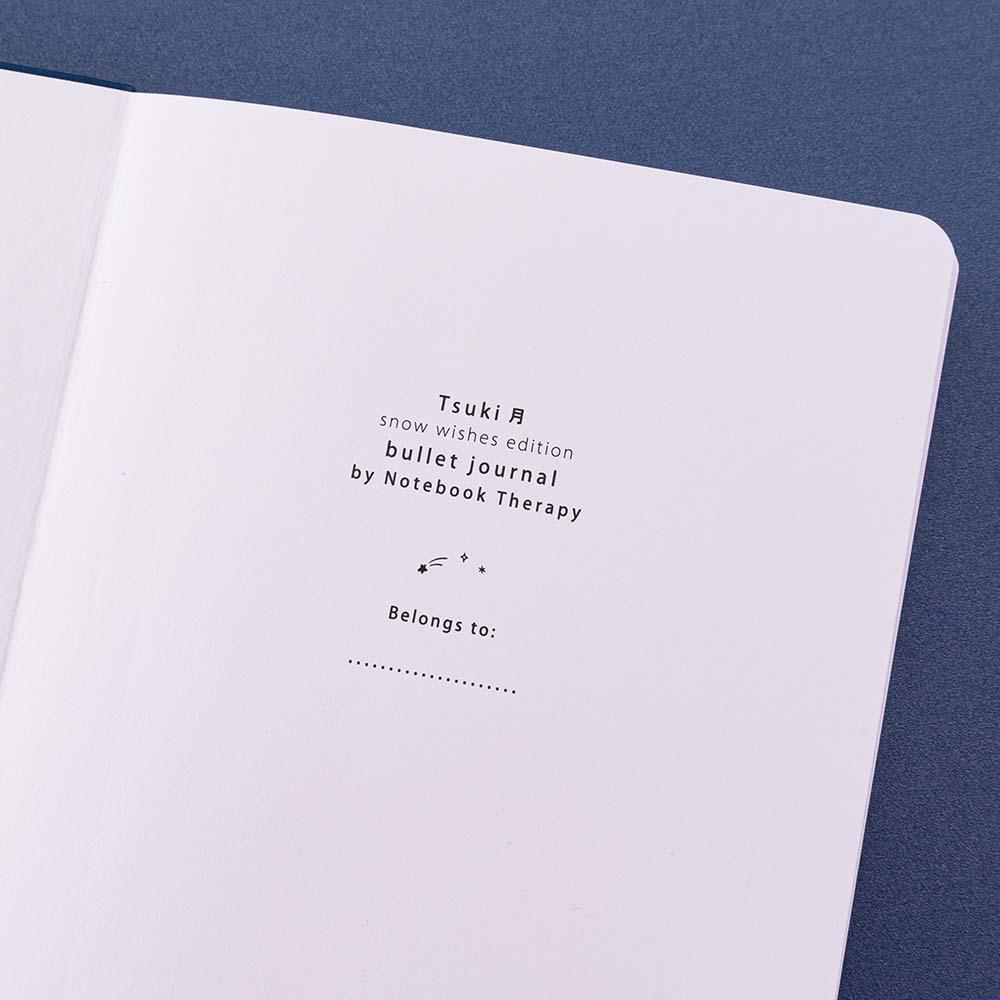 Close up of open front page of Tsuki ‘Winter Wishes’ Limited Edition Bullet Journal on navy background