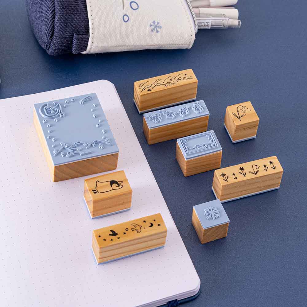 Close up of Tsuki ‘Dreams of Snow’ Bullet Journal Stamp Set on open bullet journal spread with Tsuki ‘Dreams of Snow’ Pop-Up Pencil Case in Starry Night on navy background