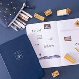 Tsuki ‘Dreams of Snow’ Bullet Journal Stamps on open bullet journal spread with Tsuki ‘Winter Wishes’ Limited Edition Bullet Journal and Tsuki ‘Dreams of Snow’ Pop-Up Pencil case in Starry Night on navy background