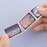 Tsuki ‘Dreams of Snow’ Holographic Stamp Washi Tape held in hands in light blue background