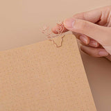 Close up of open page of Tsuki Kraft Paper Limited Edition Bullet Journal in Nara with free bookmark gift held in hand on beige background