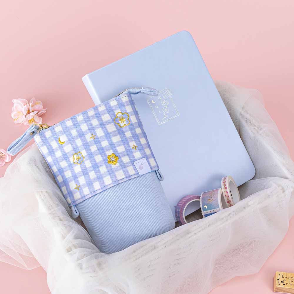 Tsuki ‘Sakura Journey’ Pop-Up Pencil Case with Tsuki ‘Sakura Journey’ Limited Edition Bullet Journal and Tsuki ‘Sakura Journey’ Washi Tapes in netted basket with cherry blossoms and Tsuki ‘Sakura Journey’ Bullet Journal Stamp on light pink background