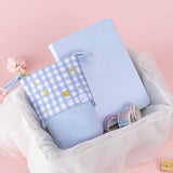 Tsuki ‘Sakura Journey’ Pop-Up Pencil Case with Tsuki ‘Sakura Journey’ Limited Edition Bullet Journal and Tsuki ‘Sakura Journey’ Washi Tapes in netted basket with cherry blossoms and Tsuki ‘Sakura Journey’ Bullet Journal Stamp on light pink background