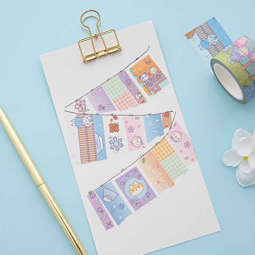 Close up of Tsuki ‘Four Seasons’ Washi Tapes by Notebook Therapy x Milkkoyo on white card clipboard with gold pen and white flower on light blue background