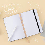 Opened bullet journal on yellow background with words 160gsm white pages in white writing