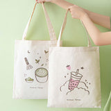 Tsuki ‘Matcha Matcha’ Tote Bag held in hands with Tsuki ‘Ichigo’ Boba Tote Bag in matcha green background
