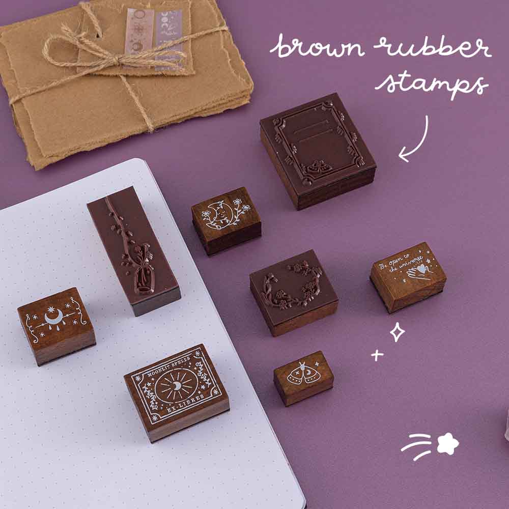 Close up of Tsuki ‘Moonlit Spells’ Bullet Journal Stamps with brown rubber material near open bullet journal page with scrapbook paper on purple background