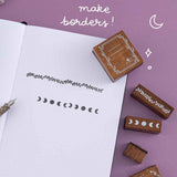 Close up of ope bullet journal page with Tsuki ‘Moonlit Spells’ Bullet Journal Stamps you can make borders with, with quill pen on purple background