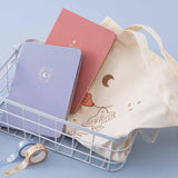 Tsuki ‘Moonflower’ Limited Edition Tote Bag with ‘Suzume’ Limited Edition Bullet Journal and ‘Full Bloom’ Limited Edition Notebook and ‘Moonflower’ Washi Tapes in basket on light blue background