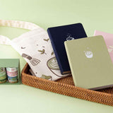 Tsuki ‘Matcha Matcha’ Tote Bag with Tsuki ‘Ichigo’ Limited Edition Boba Bullet Journal and Tsuki ‘Cup of Galaxy’ Limited Edition Holographic Bullet Journal and Tsuki ‘Matcha Matcha’ Limited Edition notebook and Tsuki ‘Matcha Ichigo’ Washi Tape Set in brown basket on beige linen covered table