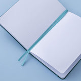 Sea green velvet Tsuki Dolphin Days bullet journal on open page with two bookmark ribbons on blue background