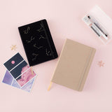 Flatlay of black and beige constellations bullet journals with star-shaped paperclips in gold and rose gold