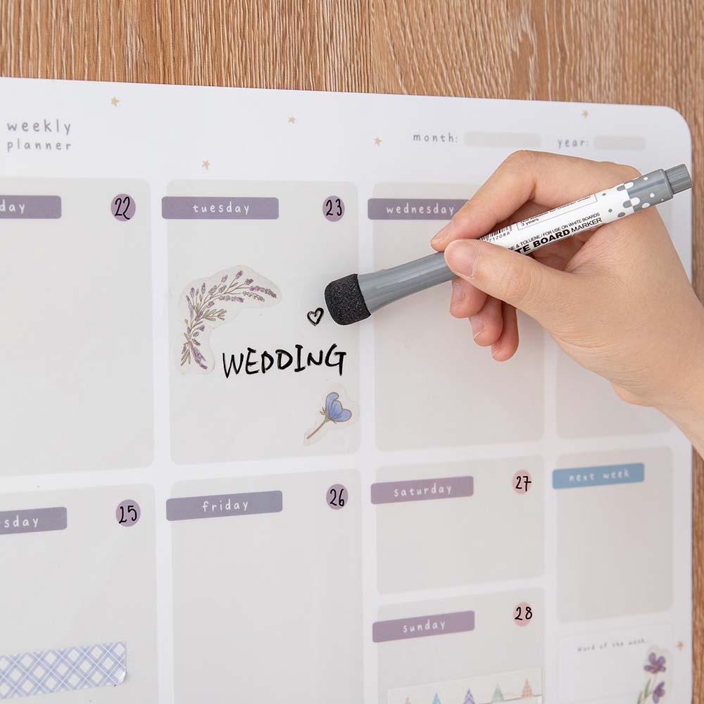 Tsuki Reusable Weekly with dry erase marker held in hands on smooth wooden surface