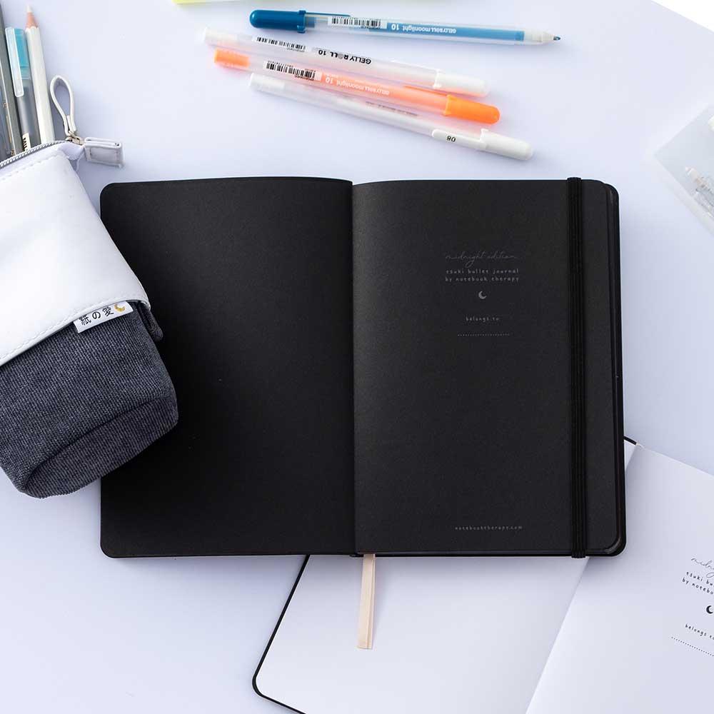Open Tsuki Black Paper Limited Edition Hardcover Bullet Journal with Gelly Roll Pens and Tsuki Pop-Up Pencil Case in charcoal and open white page bullet journal on white background