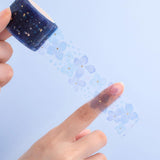 Tsuki Endless Summer Washi matte transparent floral tape roll held in hands on light blue background