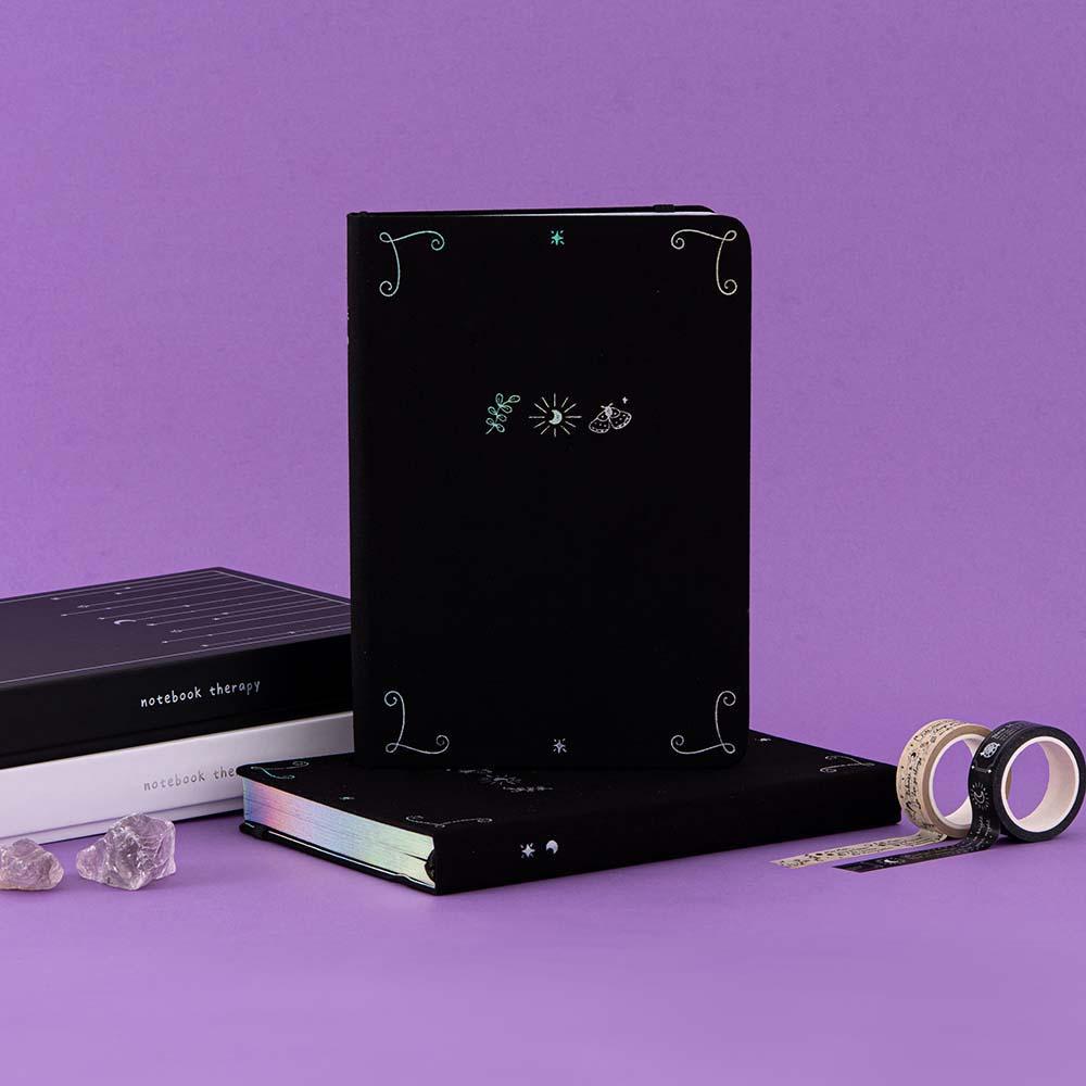 Tsuki ‘Moonlit Spell’ Limited Edition Holographic Bullet Journals in white and black paper variations with eco-friendly gift boxes with Tsuki ‘Moonlit Spell’ Washi Tapes with amethyst stones in purple background  Edit alt text