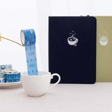 Tsuki ‘Cup of Galaxy’ Washi Tapes in teacup and on saucer with Tsuki ‘Cup of Galaxy’ Limited Edition Holographic Bullet Journal and Tsuki ‘Matcha Matcha’ Limited Edition notebook on linen covered table