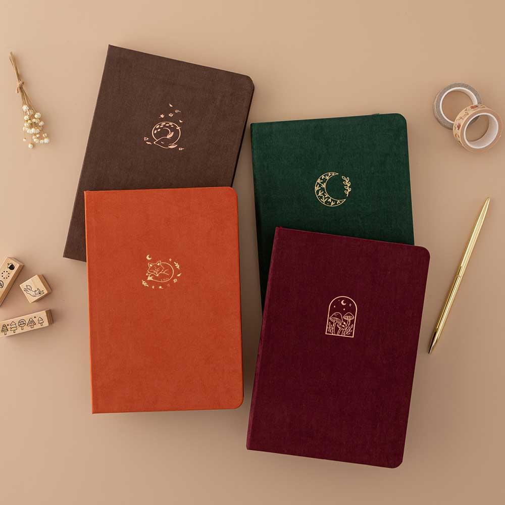 Tsuki ‘Kitsune’ Limited Edition Fox Bullet Journal and Tsuki ‘Nara’ Limited Edition Bullet Journal and Tsuki ‘Kinoko’ Limited Edition Bullet Journal and Tsuki ‘Midnight Garden’ Limited Edition Bullet Journal with Tsuki ‘Maple Dreams’ Washi Tapes and Tsuki ‘Maple Dreams’ Bullet Journal Stamps with gold pen and dried flowers on beige background