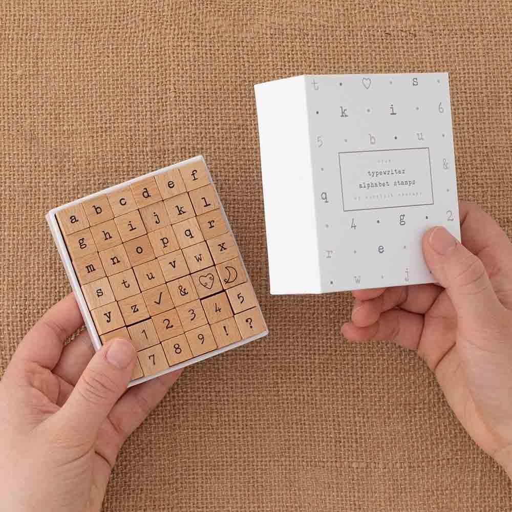 Tsuki Bullet Journal Typewriter Style Alphabet Stamps with eco-friendly gift box packaging held in hands at an angle on hessian background