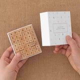 Tsuki Bullet Journal Typewriter Style Alphabet Stamps with eco-friendly gift box packaging held in hands at an angle on hessian background