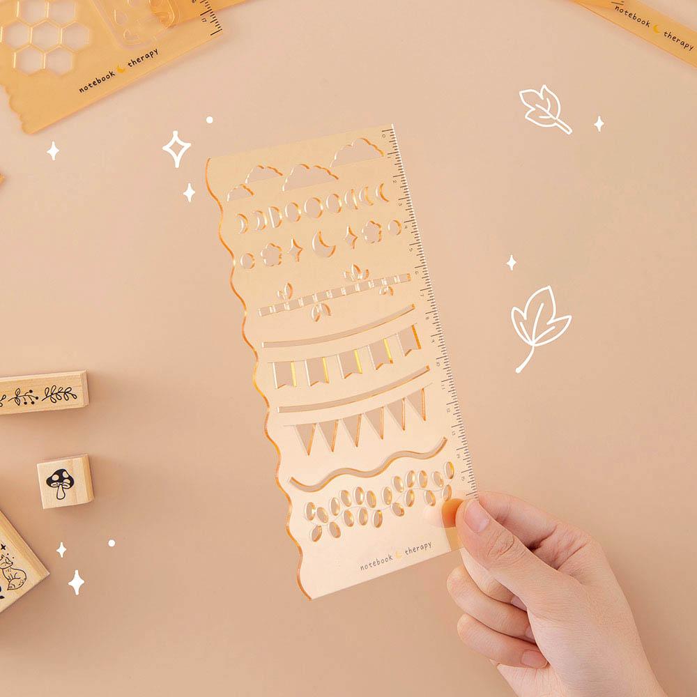 Tsuki Bullet Journal Stencil Set in neutral held in hand at an angle withTsuki ‘Maple Dreams’ Bullet Journal Stamps in beige background