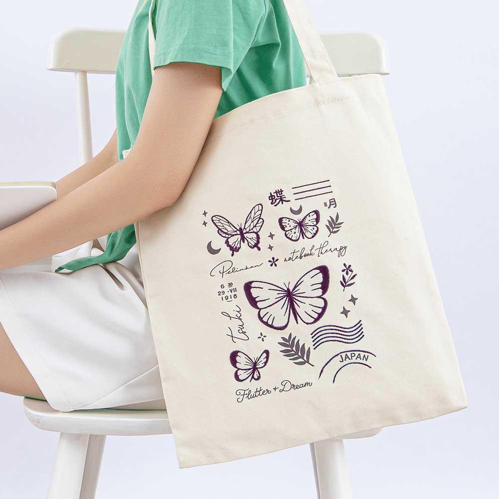 Tsuki ‘Flutter + Dream’ Tote Bag by Notebook Therapy x Pelinkan on model’s arm in light grey background