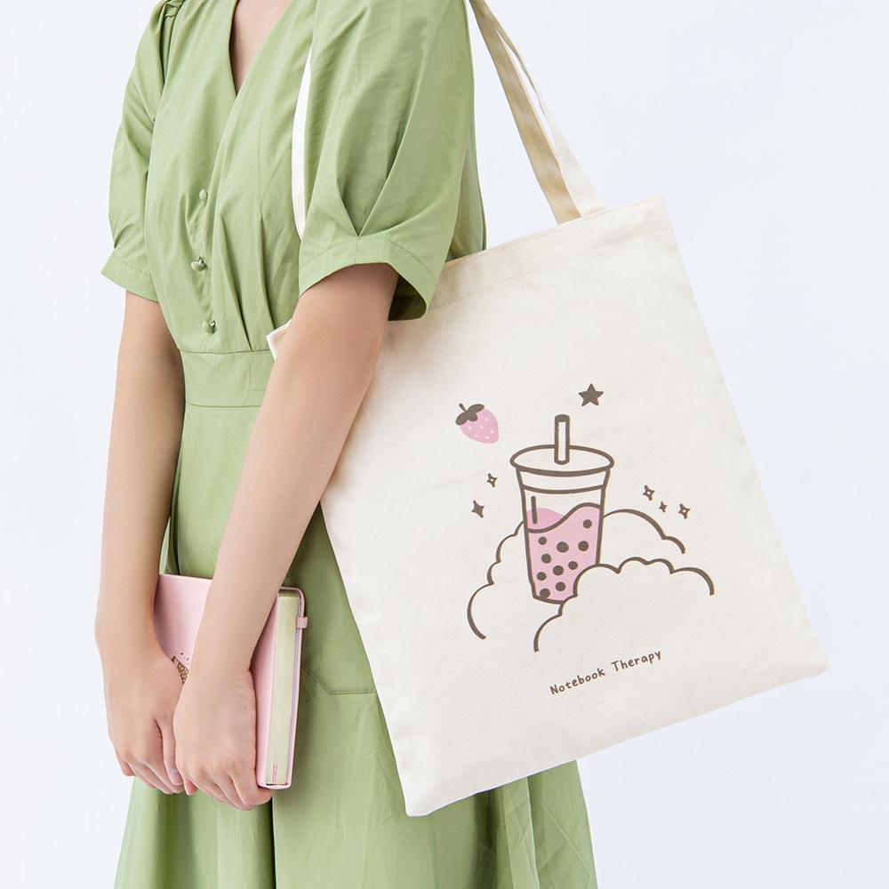 Tsuki ‘Ichigo’ Boba Tote Bag shown on model’s arm with Tsuki ‘Ichigo’ Limited Edition Boba Bullet Journal in arms in light grey background