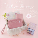 Tsuki ‘Sakura Journey’ Vintage Journal Washi Tape Set with Tsuki ‘Sakura Journey’ Limited Edition Travel Notebook and Tsuki ‘Sakura Journey’ Scrapbooking Set’ and Tsuki ‘Sakura Journey’ Travel Pouch in basket with cherry blossoms in pink background