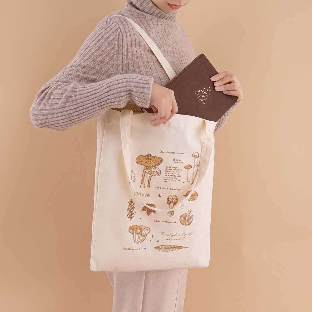 Tsuki ‘Vintage Kinoko’ Tote Bag held open on model’s arm with Tsuki ‘Nara’ Limited Edition Bullet Journal inside in beige background