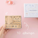 Tsuki ‘Four Seasons’ Bullet Journal Stamp Set by Notebook Therapy x Milkkoyo with ten stamps held in hand with pink flower in petal pink background