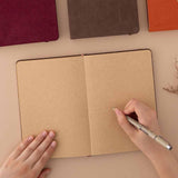 Open Tsuki Kraft Paper Limited Edition Bullet Journal with pen held in hands with Tsuki ‘Kitsune’ Limited Edition Fox Bullet Journal and Tsuki ‘Nara’ Limited Edition Bullet Journal and Tsuki ‘Kinoko’ Limited Edition Bullet Journal on beige background