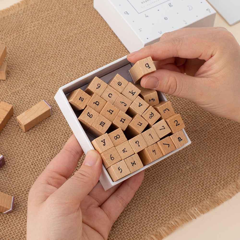 Close up of Tsuki Bullet Journal Typewriter Style Alphabet Stamps held in hands at an angle on hessian mat in beige background