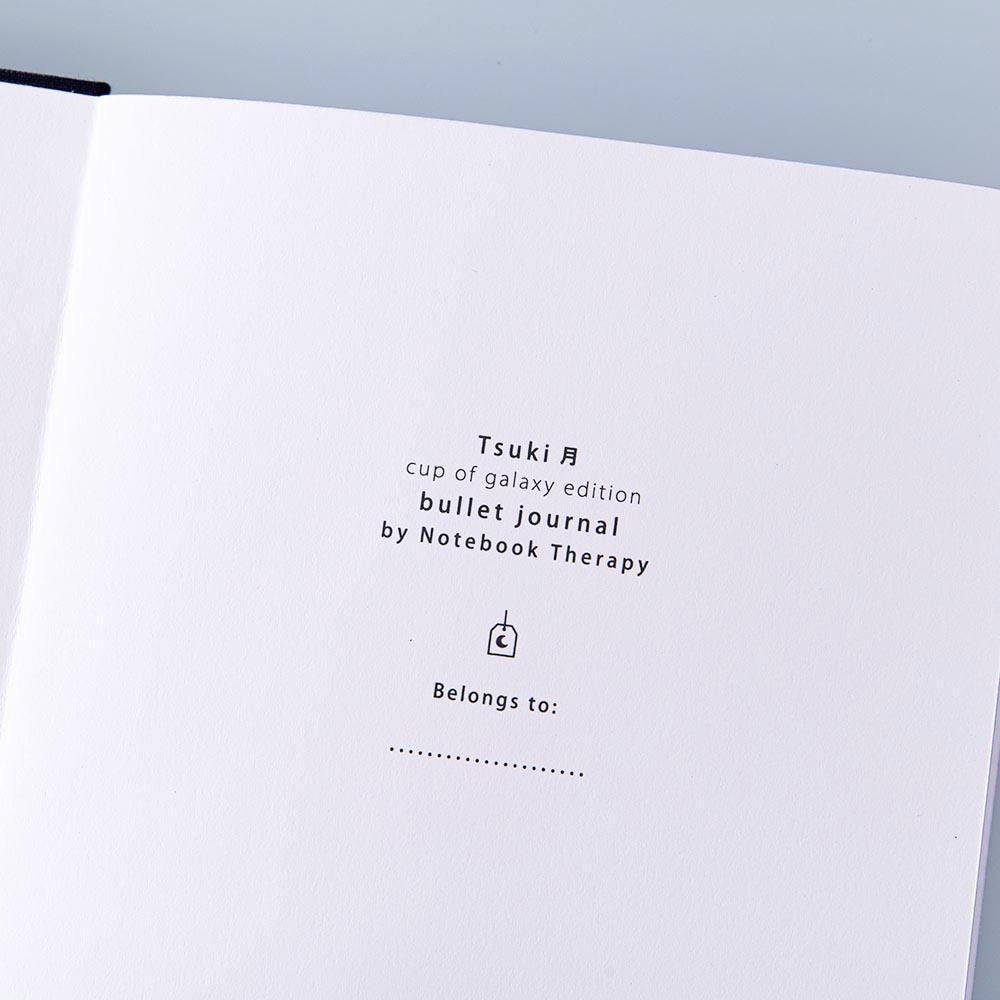 Close up of the open front page of Tsuki ‘Cup of Galaxy’ Limited Edition Holographic Bullet Journal on light blue background