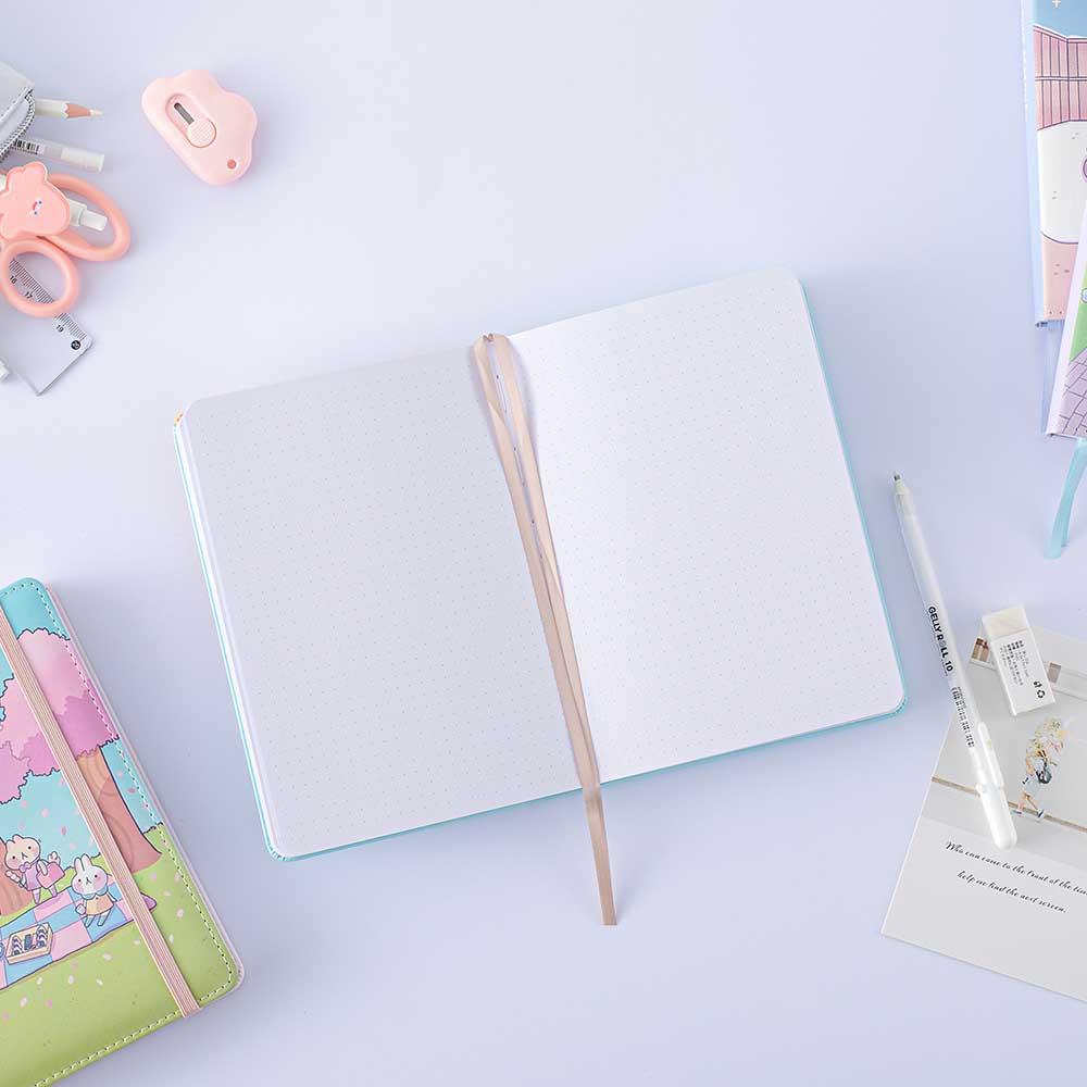 Open page spread of Tsuki ‘Four Seasons: Autumn Edition’ Bullet Journal made with milkkoyo with Tsuki ‘Four Seasons: Summer Edition’ notebook with assorted stationery supplies on lilac background