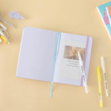 Tsuki Four Seasons: Summer Edition Bullet Journal designed with @milkkoyo on open page with pens and postcard and Tsuki Four Seasons: Spring Edition notebook on honey yellow background