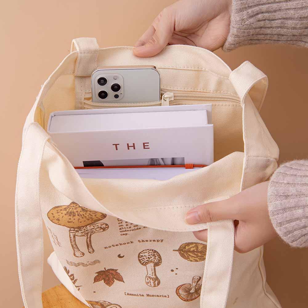 Open Tsuki ‘Vintage Kinoko’ Tote Bag with book and mobile phone and Tsuki ‘Kitsune’ Limited Edition Fox Bullet Journal inside held in hands in beige background