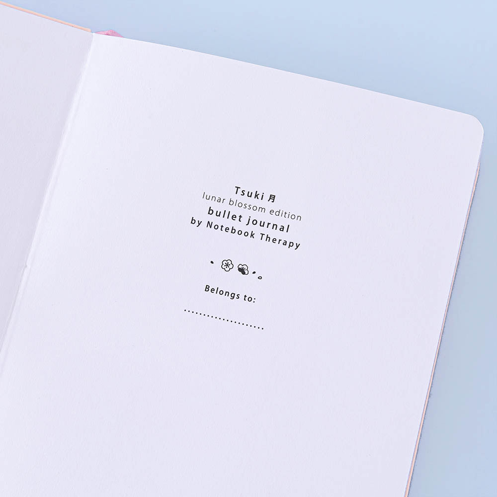 Close up of open front page of Tsuki ‘Lunar Blossom’ Limited Edition Bullet Journal on light blue background