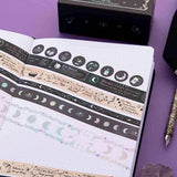 Close up of Tsuki ‘Moonlit Spell’ Washi Tapes rolled out on open Tsuki ‘Moonlit Spell’ Limited Edition Holographic Bullet Journal page with black feather quill on purple background