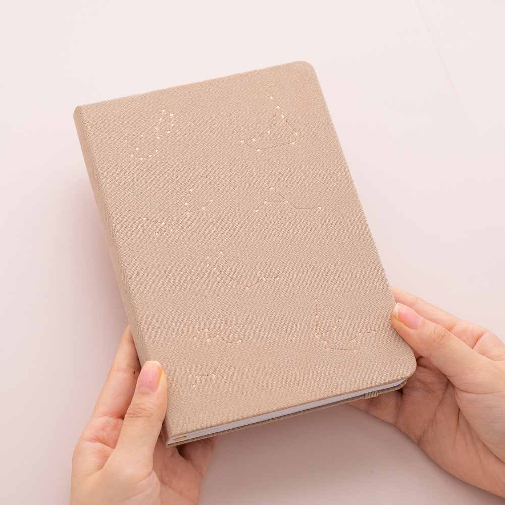 Hands holding tsuki constellations bullet journal in soft moondust beige