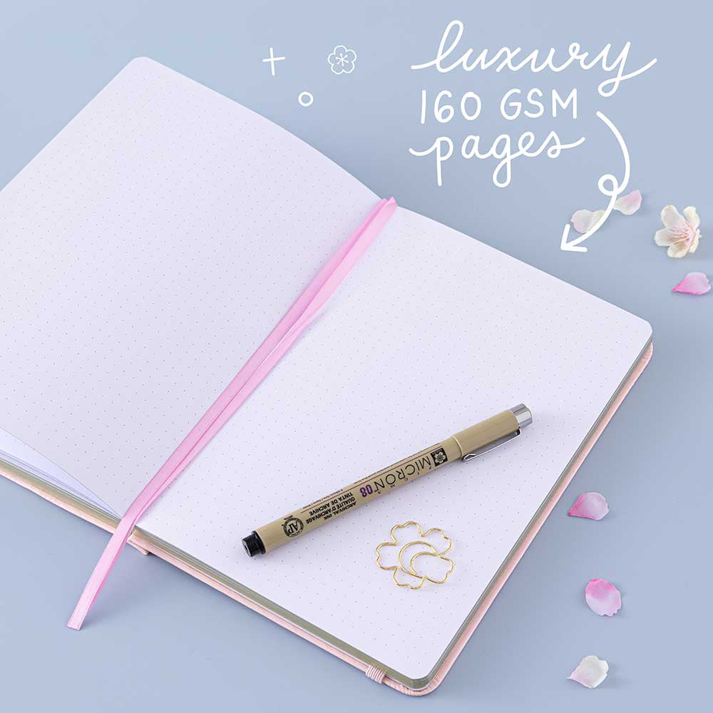 Open page of Tsuki ‘Lunar Blossom’ Limited Edition Bullet Journal with luxury 160GSM pages pen with cherry blossom petals on light blue background